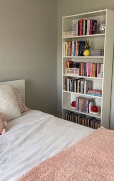 a bedroom with a bed, bookshelf and stuffed animal on the pillow in it