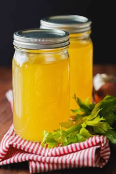 two jars filled with yellow liquid sitting on top of a wooden table next to a red and white napkin