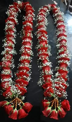 red and white flowers are arranged on a black surface with beads in the middle, along with pearls