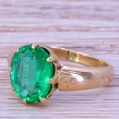 an oval shaped green stone sits in the center of a gold ring on a wooden surface