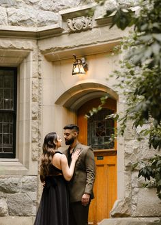 a man and woman are standing in front of a building with a wooden door, looking into each other's eyes