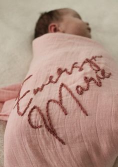 a baby wrapped in a pink blanket with writing on it