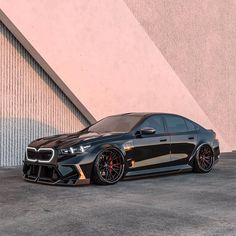 a black sports car parked in front of a building with red rims on it