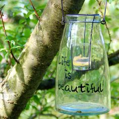 a glass jar hanging from a tree branch with words written on it that read life is beautiful