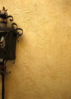 a black clock on the side of a wall in front of a yellow stucco wall