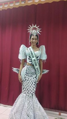 a woman in a white and black dress standing next to a red curtain wearing a tiara