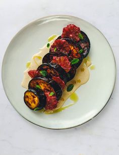 a white plate topped with grilled eggplant covered in sauce and garnish