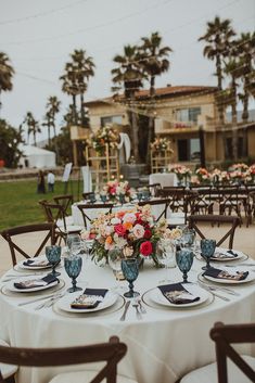 the table is set with plates and place settings for an outdoor dinner party in front of palm trees