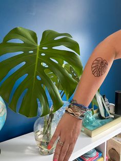 a woman's arm with a tattoo on it and a plant in the background