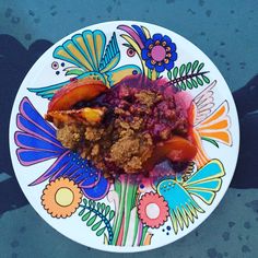 a white plate topped with fruit and crumbs on top of a blue table