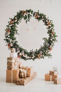 presents are stacked in front of a wreath with pine cones and flowers on it,