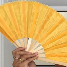 a woman holding a yellow fan in front of her face