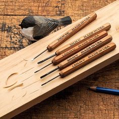 six wood carving tools are sitting on a wooden board with a bird perched on it