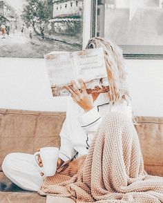 a woman sitting on a couch reading a book and holding a coffee cup in her hand