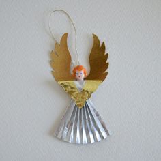 an angel ornament hanging from a string on a white wall with gold foil