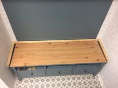 a wooden bench sitting on top of a tiled floor next to a blue and white wall