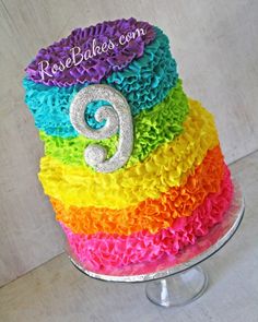 a multi - colored cake with the number nine on top and rainbow ruffles