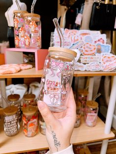 a person holding up a glass cup in front of shelves with other items on it