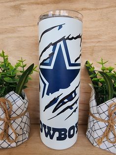 a white tumbler with the word cowboys on it next to two potted plants