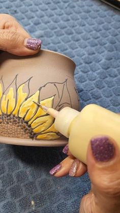 a woman is painting a sunflower on a vase with yellow and purple nail polish