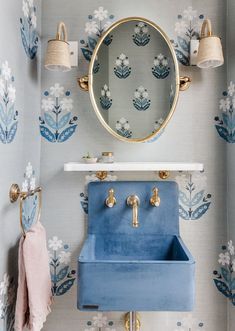 a bathroom with blue and white wallpaper, gold fixtures and a mirror above the sink