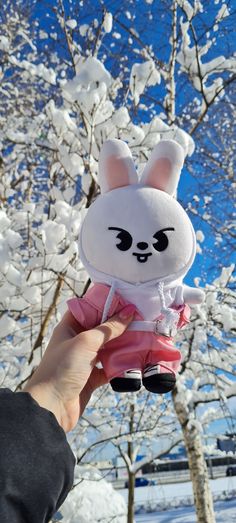 a person holding up a stuffed animal in front of snow covered trees