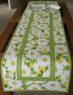 a table with a green and white flowered cloth on it, along with a bowl