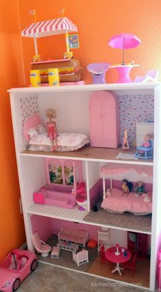 a doll house with pink furniture and accessories on the shelves in front of an orange wall