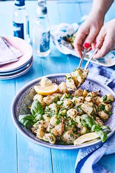 a woman is cutting into a salad with lemons and parsley on the side