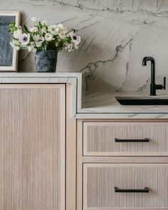 a vase with flowers sitting on top of a wooden cabinet next to a sink and faucet