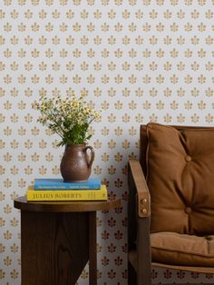 a vase with flowers sitting on top of a table next to a chair and wallpaper