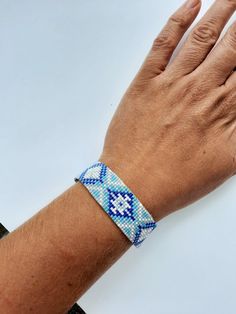 a person's hand with a blue and white beaded bracelet on their wrist