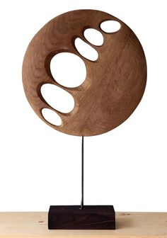 a wooden sculpture with holes in the center on a stand against a white background,