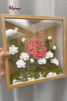 a person holding up a frame with flowers in it