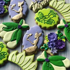 some decorated cookies on a table with flowers and leaves in the middle one cookie is green, purple, and white