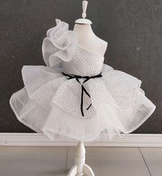 Elevate your little one's special occasion with our One Shoulder White Tutu Dress! This enchanting dress is perfect for birthdays, parties, or any celebration where your child deserves to shine. Designed with elegance and flair, it features a chic one-shoulder design and a stunning white tutu adorned with glitter. Features: Elegant One Shoulder Design: Adds a touch of sophistication and unique style. White Glittery Tutu: Sparkles beautifully, making your toddler the star of any event. Comfortabl Elegant Ruffled Baptism Dress For Party, Fitted Princess Style Baptism Dress For Party, Elegant Ruffled Princess Dress For Birthday, Elegant Princess Dress For Birthday Party Season, Elegant Princess Dress In Glitter Tulle For Party Season, Elegant Ruffled Tutu Dress For Birthday, White Ruffled Princess Dress For Baptism, Elegant White Pageant Dress For Baptism, White Elegant Pageant Dress With Ruffles