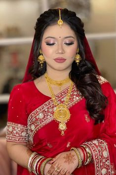 a woman wearing a red and gold bridal outfit with her hands on her chest