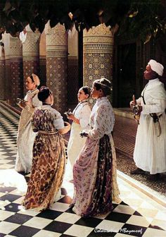 four women in long dresses standing on a checkerboard floor with one woman looking up at the sky