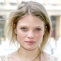 a close up of a person wearing a necklace and looking at the camera with a serious look on her face