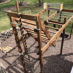 a wooden playground structure with ropes on the top and bottom, surrounded by graveled ground