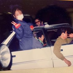 two people in a car with masks on and one person waving from the back window