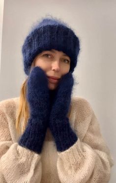 a woman wearing a blue hat and mittens is holding her hands up to her face