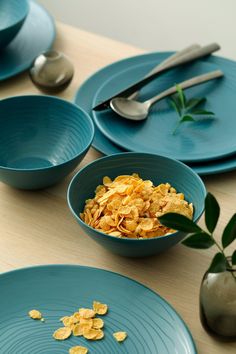 blue plates and bowls with cereal in them on a wooden table next to utensils