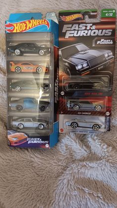 two hot wheels cars in their packaging on a bed