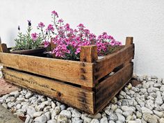 a wooden planter filled with purple flowers on top of a pile of rocks next to a white wall