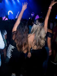 two women dancing at a party with their arms in the air