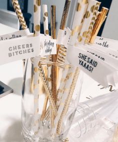 gold and white straws are in a clear glass vase on a table with tags