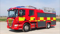 a red and yellow fire truck parked in a parking lot next to an empty field