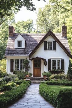 a white house with black shutters and brown trim on the front door is surrounded by greenery