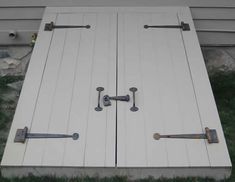 two white doors with handles and latches on the side of a house next to grass